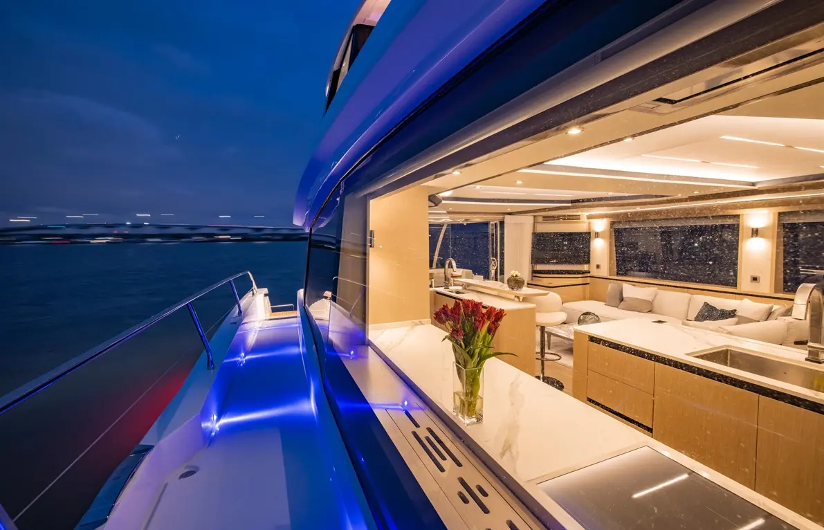 Luxurious yacht interior at night, featuring a sleek kitchen and flowers on a marble counter with blue LED lighting.